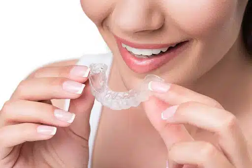 Woman holding clear Invisalign aligner used for bite and jaw correction